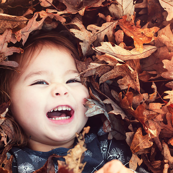 Happy toddler girl smiling while lying down in a big pile of leaves